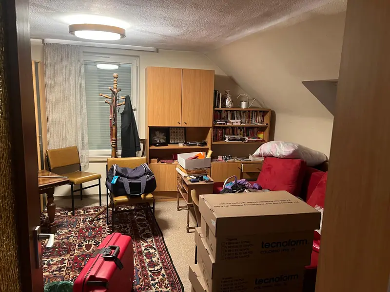 Dachzimmer mit Möbeln, Koffern und Kartons