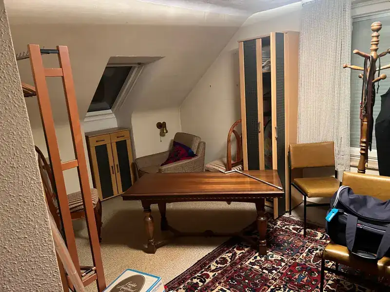 Möbliertes Dachzimmer mit Tisch, Schrank und Teppich